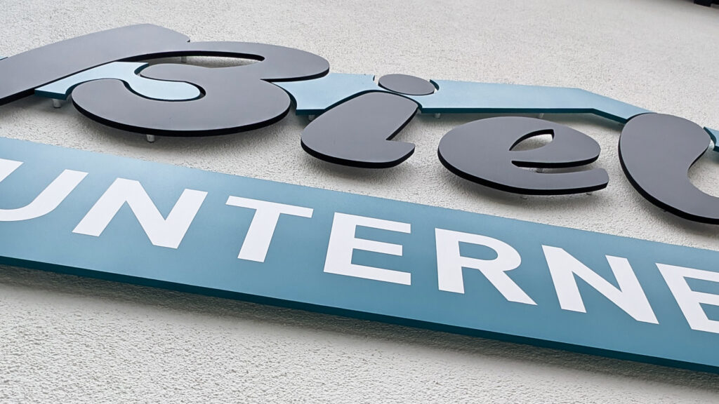 3-farbige 3D Fräsbuchstaben als Firmenlogo an einer modernen Außenfassade, professionell montiert von c&w - das Werbezentrum in Geretsried.