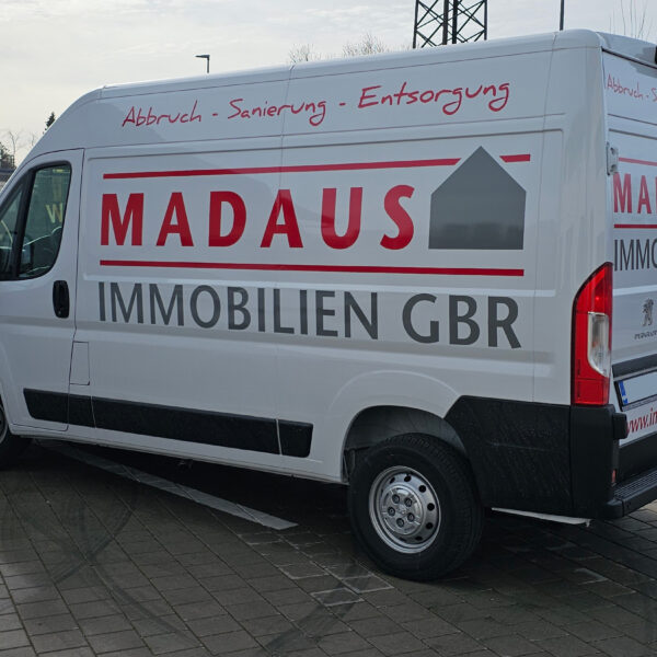 Auffällige zweifarbige Plot-Beschriftung auf einem weißen Transporter für Madaus Immobilien GbR, erstellt von c&w - das Werbezentrum in Geretsried. Das Logo und der Slogan sind prominent platziert.